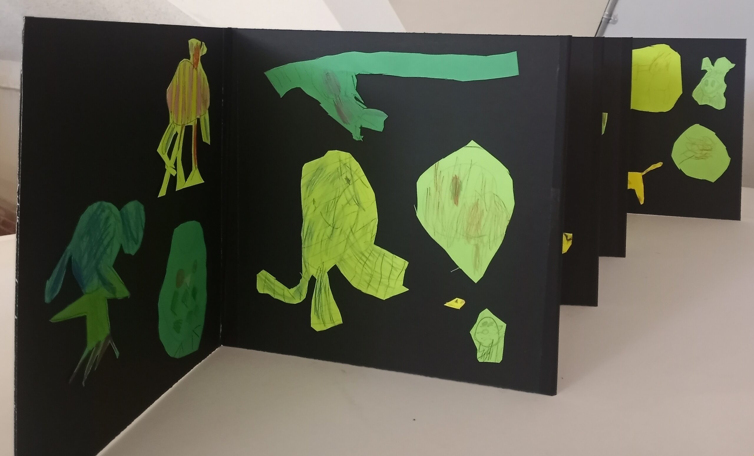 a black, accordion-folded book full of sketches done by children on varying shades of green paper