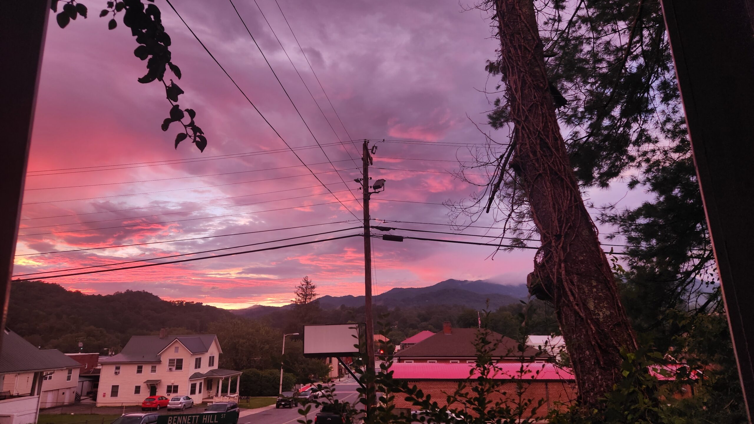 A sunset photo, with clouds illuminated pink, houses and mountains bathed in the light.